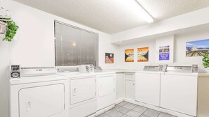 A laundry area with stacked washers and dryers, a window with blinds, and wall-mounted artwork. - Super 8 by Wyndham Grand Junction Colorado (Grand Junction)