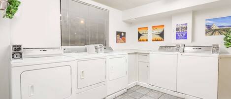 A laundry area with stacked washers and dryers, a window with blinds, and wall-mounted artwork.