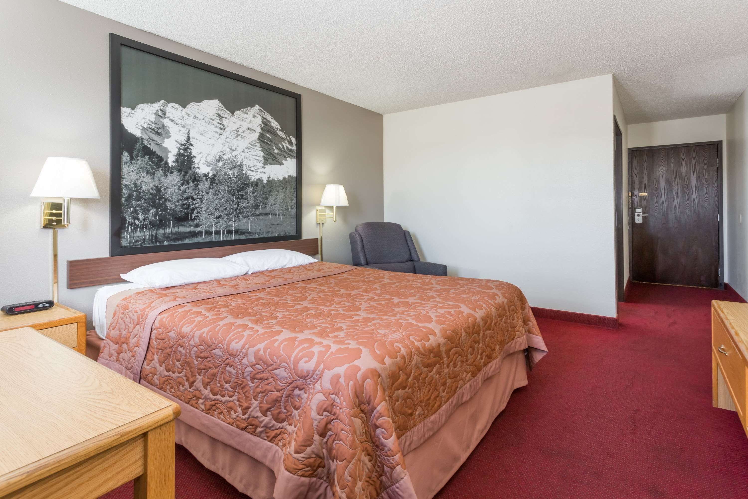 Ein Hotelzimmer mit einem großen Bett, zwei Nachttischlampen, einem Sessel, einem Schreibtisch und einer Tür.