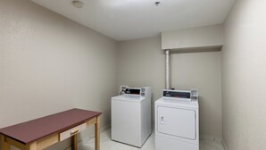 A laundry room with two front-loading washing machines and a wooden table. - Red Roof Inn Pharr - McAllen (Pharr)
