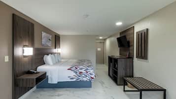 Habitación de hotel con cama, mesita de noche, escritorio, televisor y un banco.