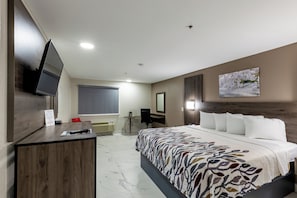 Een hotelkamer met een bed, een bureau, een televisie, een raam met zonwering en een schilderij aan de muur.