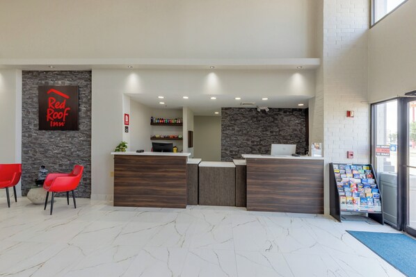 Zona de recepción de Red Roof Inn con pared de piedra, mostrador de recepción, computadora y un mueble para revistas.