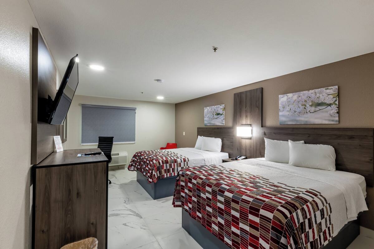 Habitación de hotel con dos camas, un escritorio, un televisor y obras de arte en las paredes.