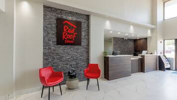 Zona de recepción de Red Roof Inn con pared de piedra, dos sillas rojas, mostrador de recepción y suelo de mármol.