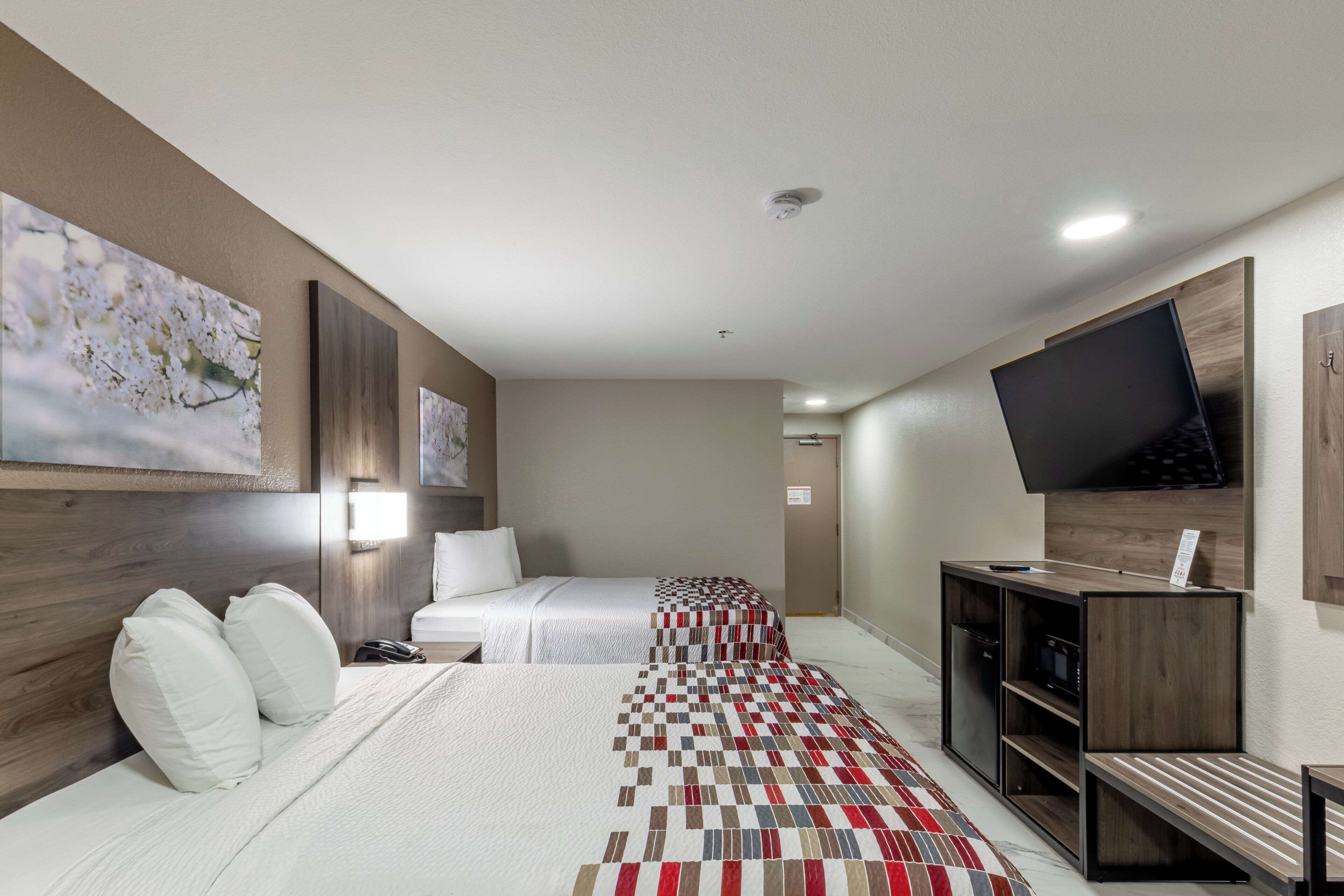 A hotel room with two beds, a TV, a desk, and artwork on the walls.
