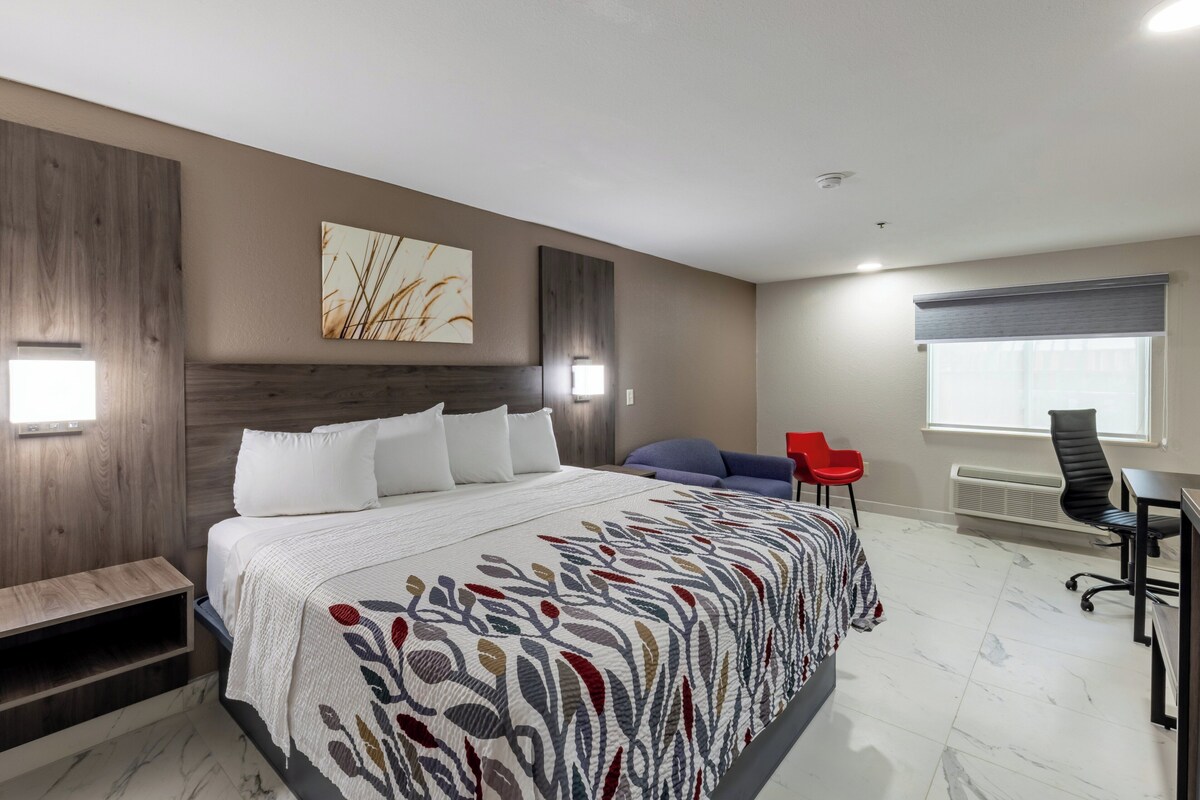A modern hotel room with a large bed, a desk, a chair, and a window.