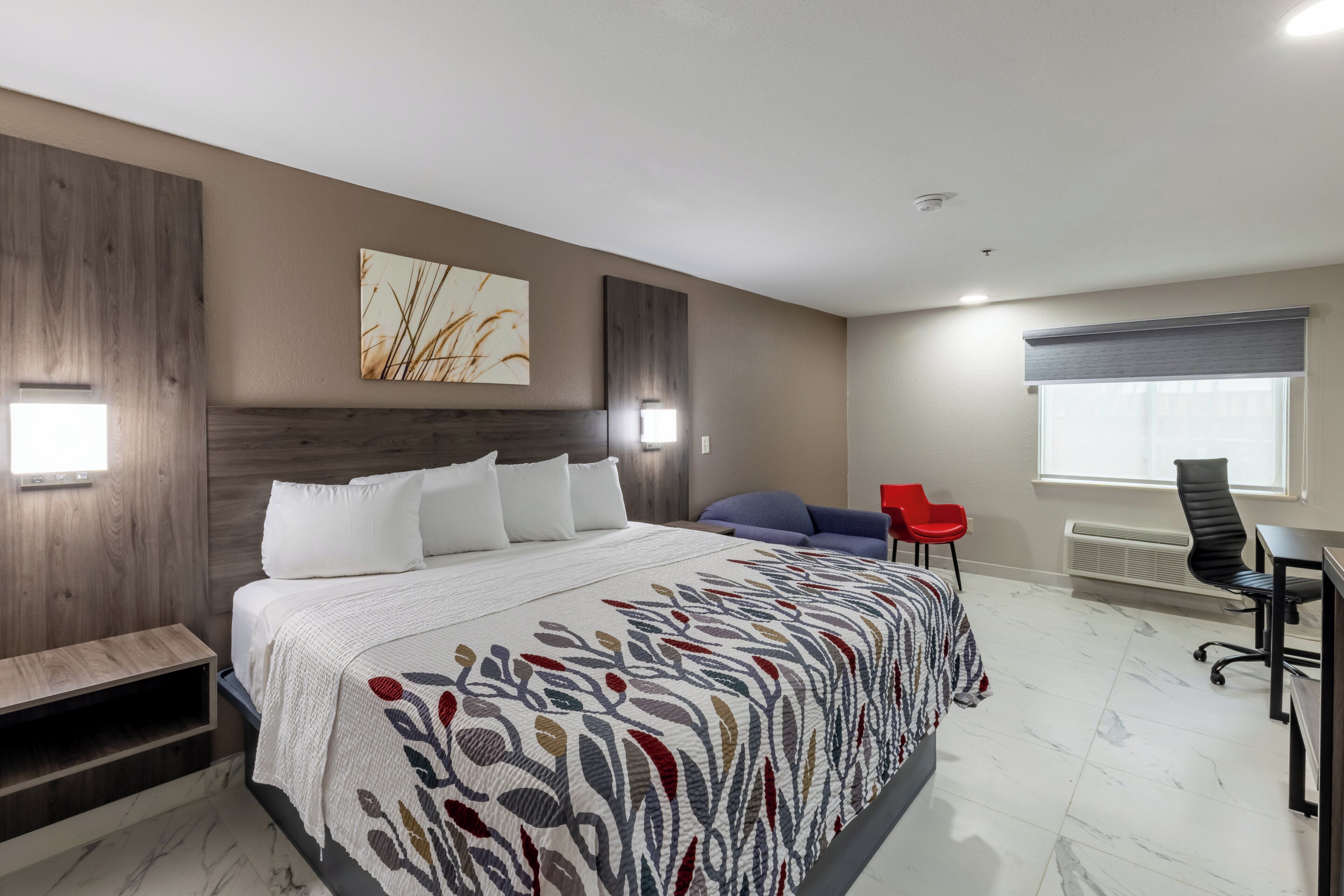 A modern bedroom with a large bed, a desk, a chair, and a window.