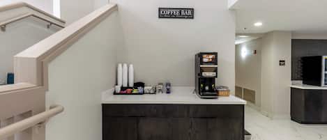 Un bar de café con un letrero encima, una máquina de café y varios artículos relacionados con el café en la barra.