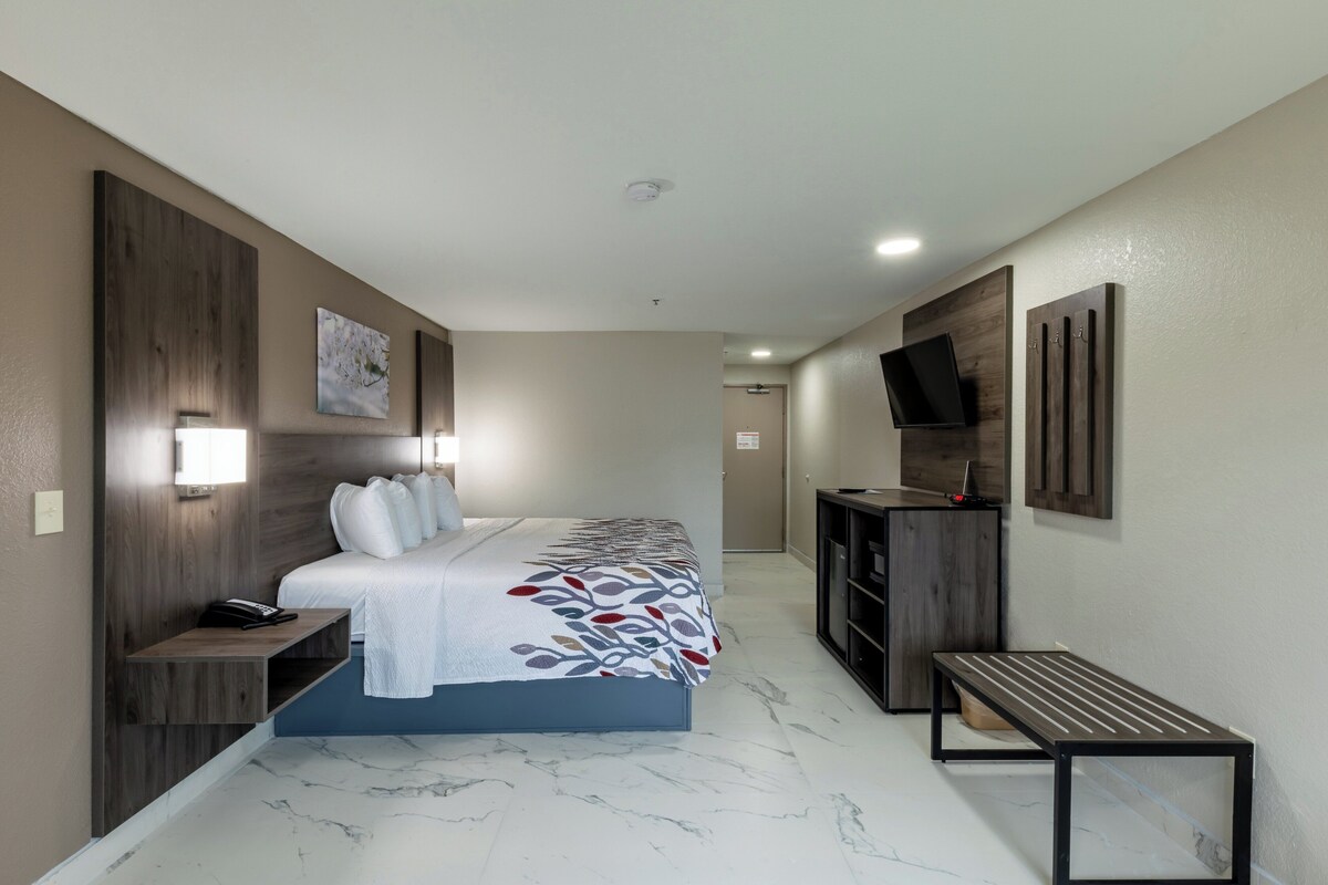 A modern hotel room with a large bed, bedside tables, a desk, a TV, and a bench.