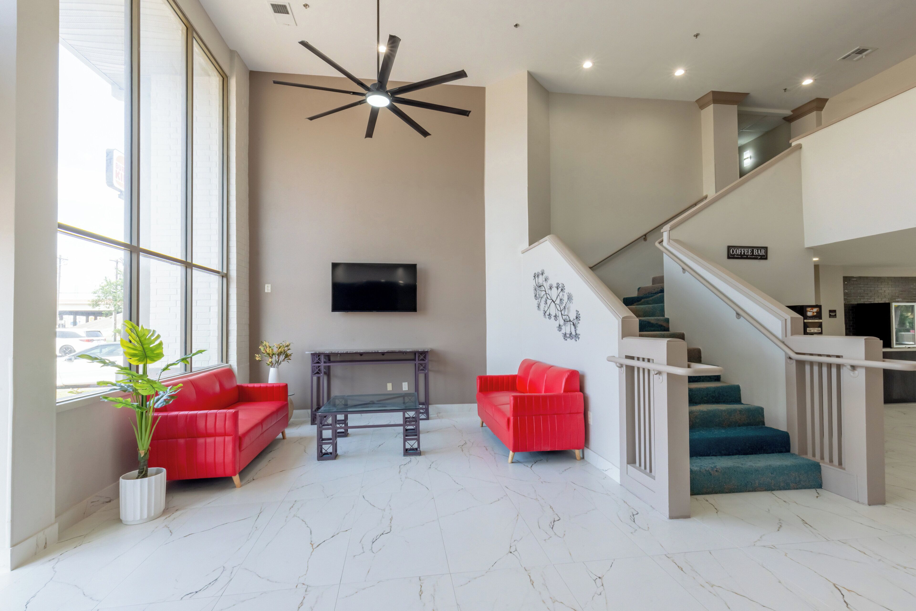 A spacious lobby with a high ceiling, a modern staircase, and a flat-screen TV mounted on the wall.