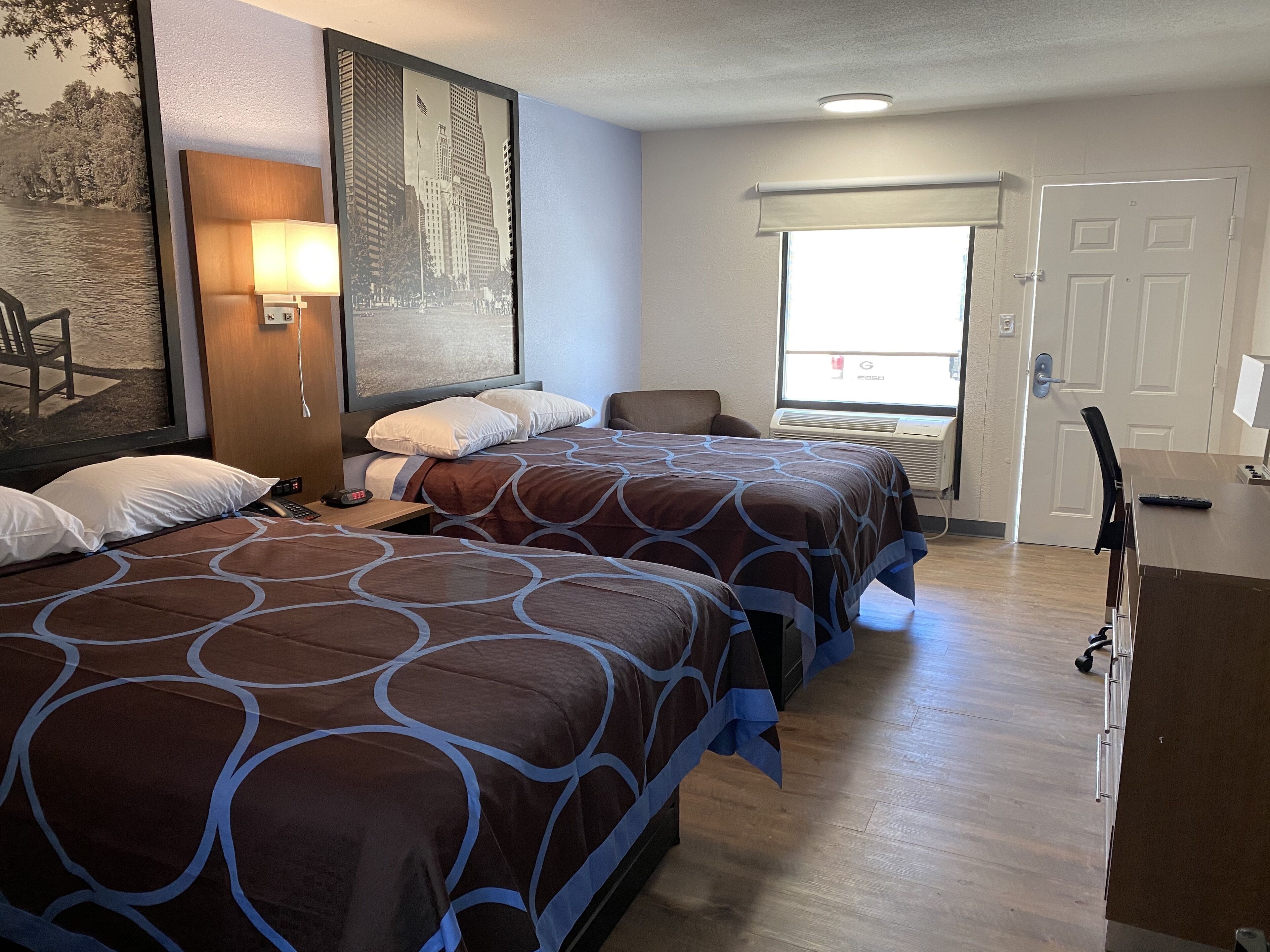 A hotel room with two beds, a desk, a chair, a window with a view, and a door.
