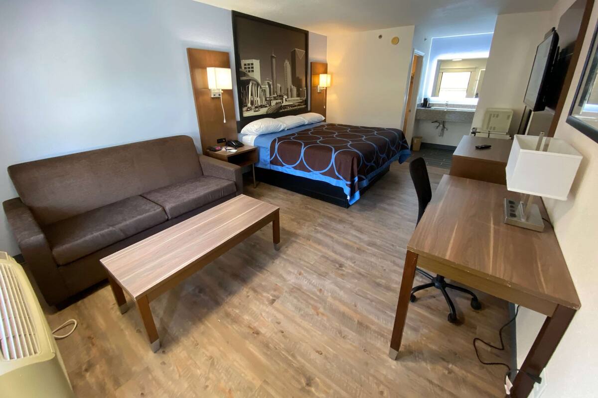 Ein Hotelzimmer mit Bett, Sofa, Schreibtisch, Stuhl, Nachttisch und einem an der Wand befestigten Fernseher.