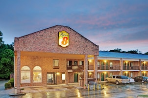 Un motel Super 8 con fachada de ladrillo, varios balcones y un estacionamiento con coches.