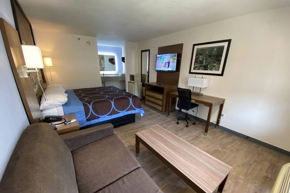 Ein Hotelzimmer mit Bett, Schreibtisch, Stuhl, Sofa, Fernseher und einer kleinen Küchenzeile.