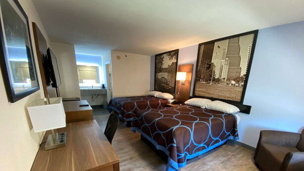 Une chambre d’hôtel avec deux lits, un bureau, une chaise, une télévision et une fenêtre.