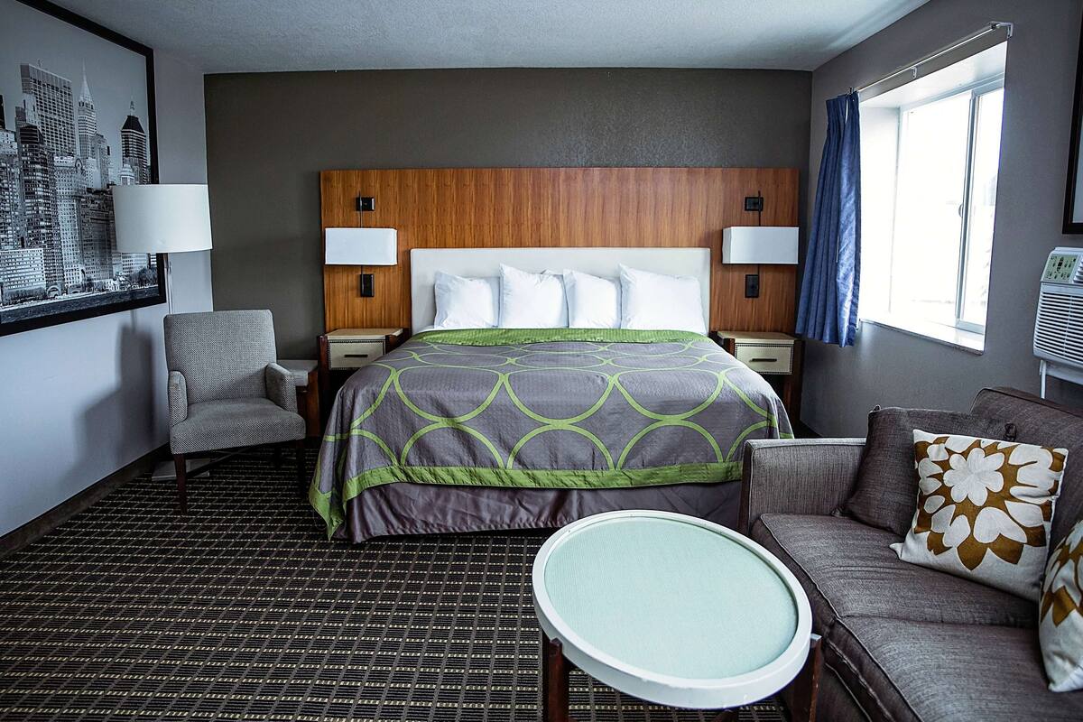 A hotel room with a bed, a chair, a sofa, a round table, and a window with curtains.