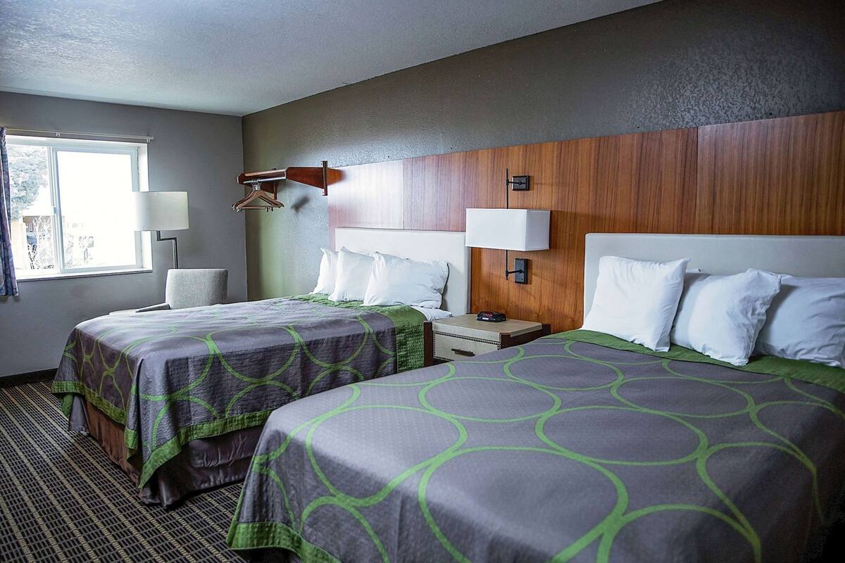 A hotel room with two beds, a wooden headboard, bedside lamps, a window, and a chair.