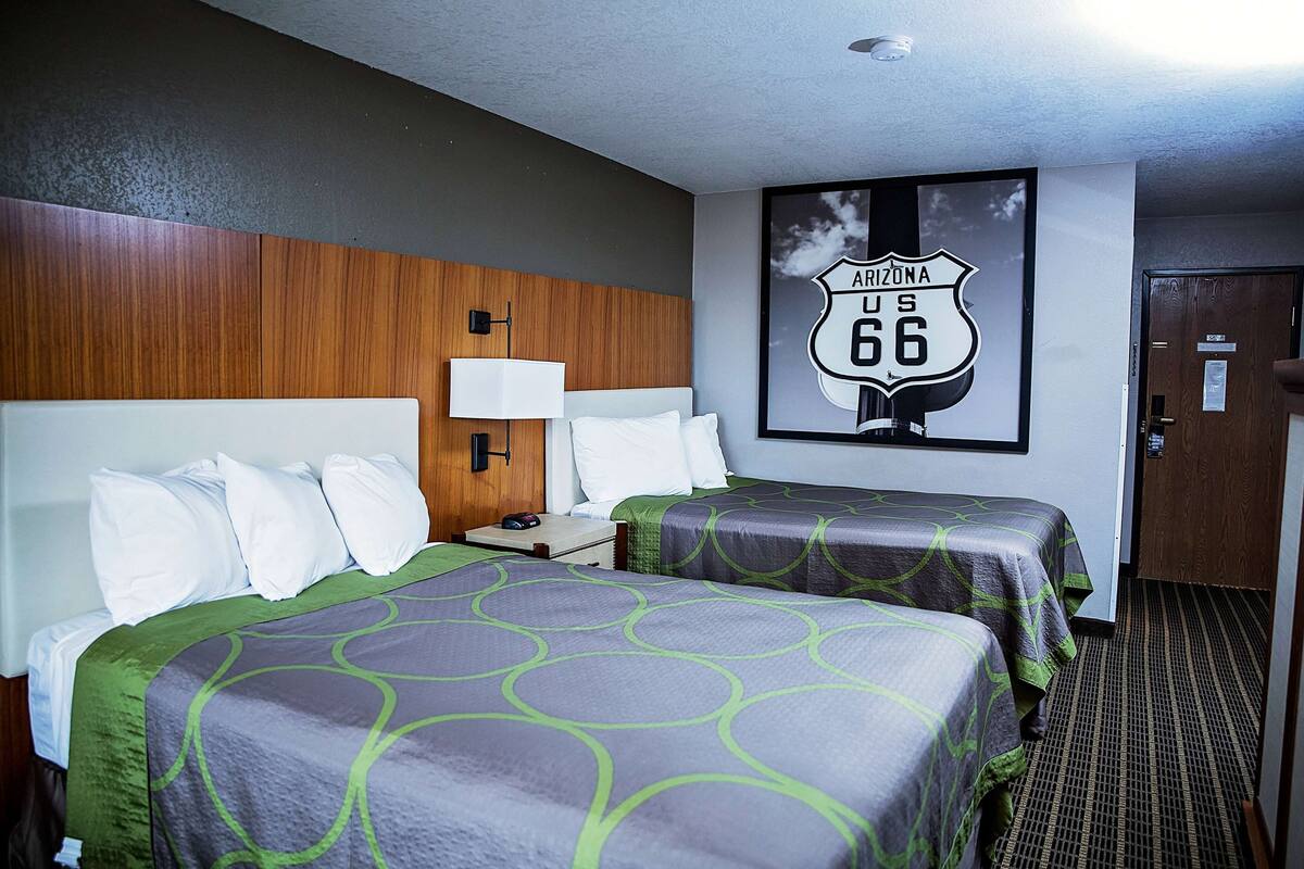 A hotel room with two beds, a wooden headboard, a nightstand, a lamp, and a framed picture of Arizona US 66 on the wall.
