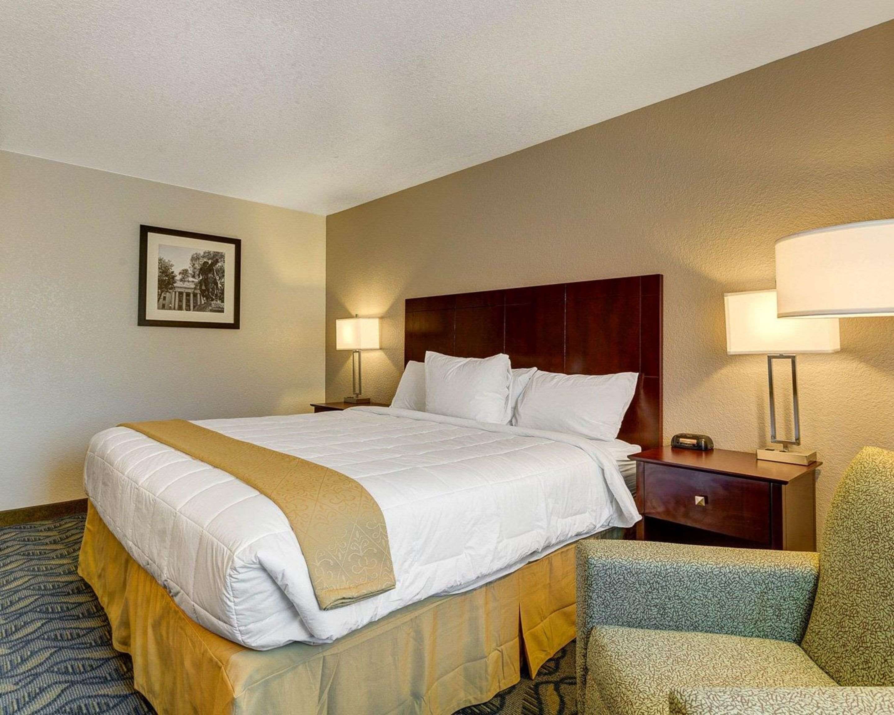 A hotel room with a large bed, two bedside tables, a chair, and a framed picture on the wall.