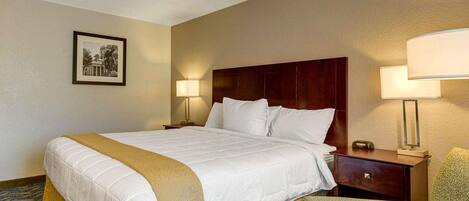 A hotel room with a large bed, two bedside tables, a chair, and a framed picture on the wall.