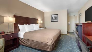 A hotel room with a large bed, two bedside tables with lamps, a TV, and a framed picture on the wall.