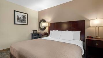 A hotel room with a large bed, a desk with a chair, a lamp, and a framed picture on the wall.