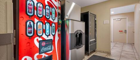 A vending machine with Coca-Cola and other beverages, a refrigerator, and a guest room door.