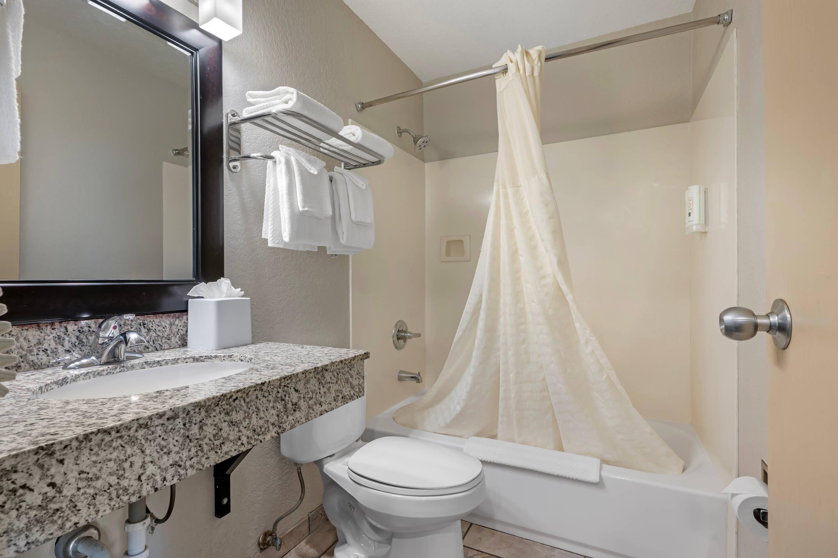 A bathroom with a granite countertop sink, a white toilet, a bathtub, and a shower curtain.
