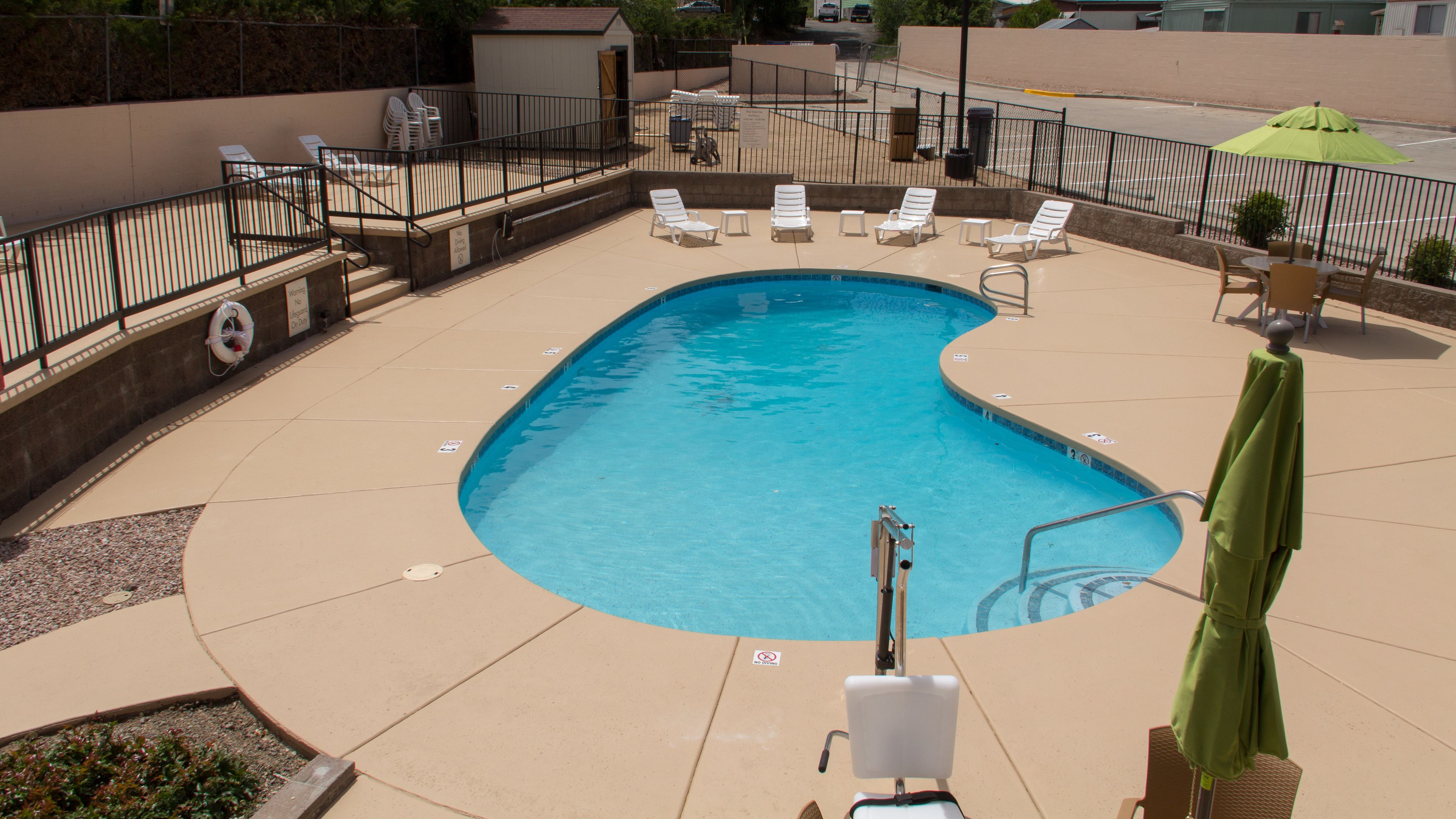 Une piscine à bord incurvé, entourée de chaises longues et d’un parasol vert.