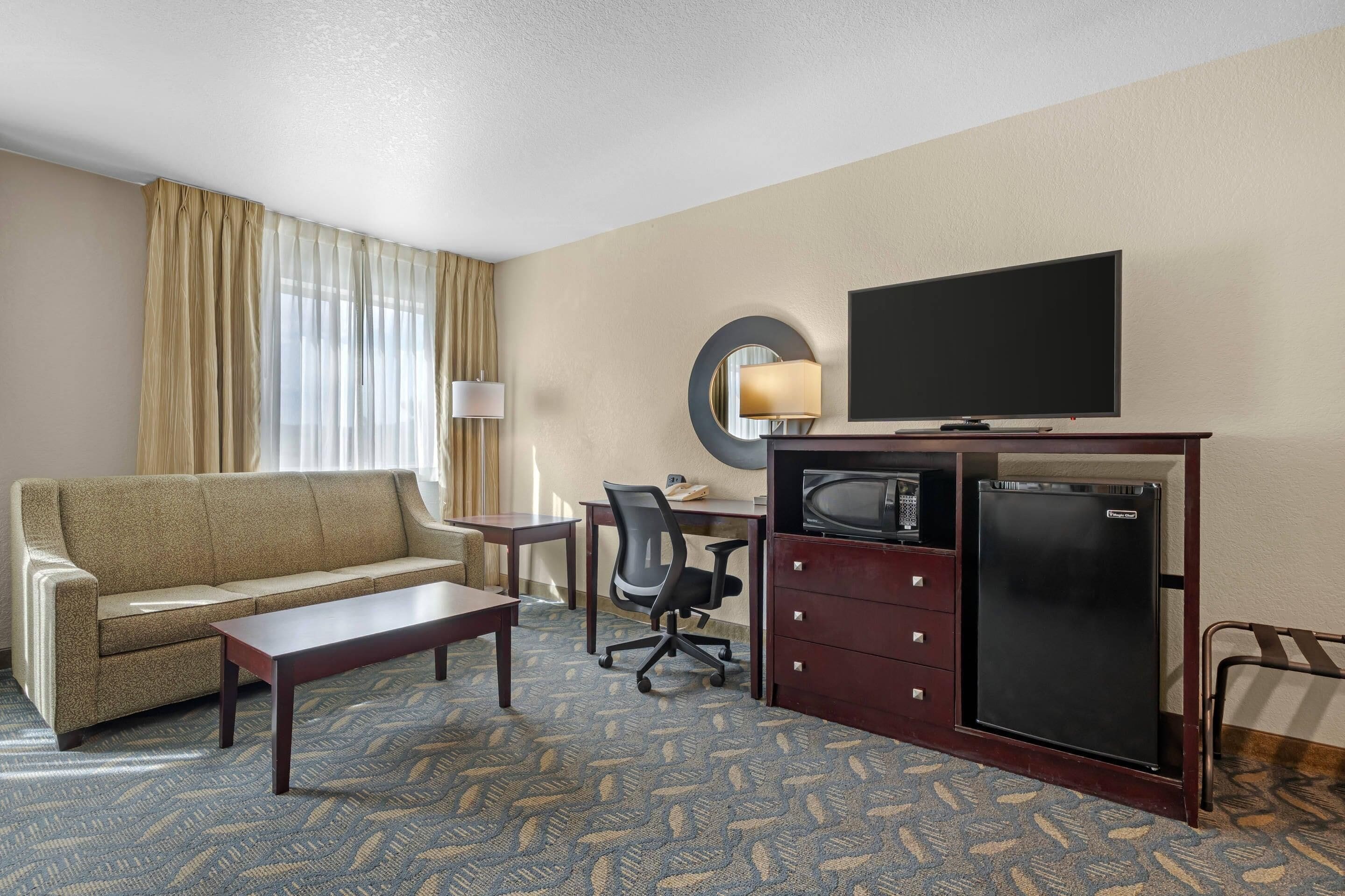 A hotel room with a sofa, a desk, a television, a refrigerator, and a patterned carpet.