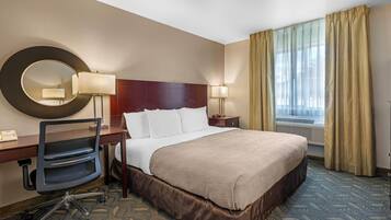 Habitación de hotel con una cama grande, un escritorio con silla, un espejo redondo, dos lámparas de noche y una ventana con cortinas.