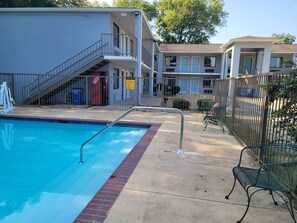 A swimming pool with a metal ladder, a covered area with a staircase, and a fenced patio with chairs.