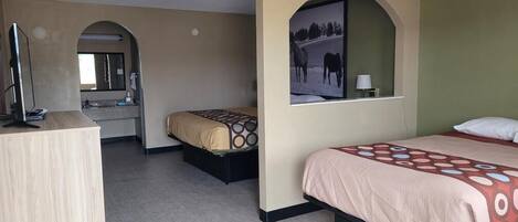 A hotel room with a desk, two beds, a mirror, and a framed picture on the wall.