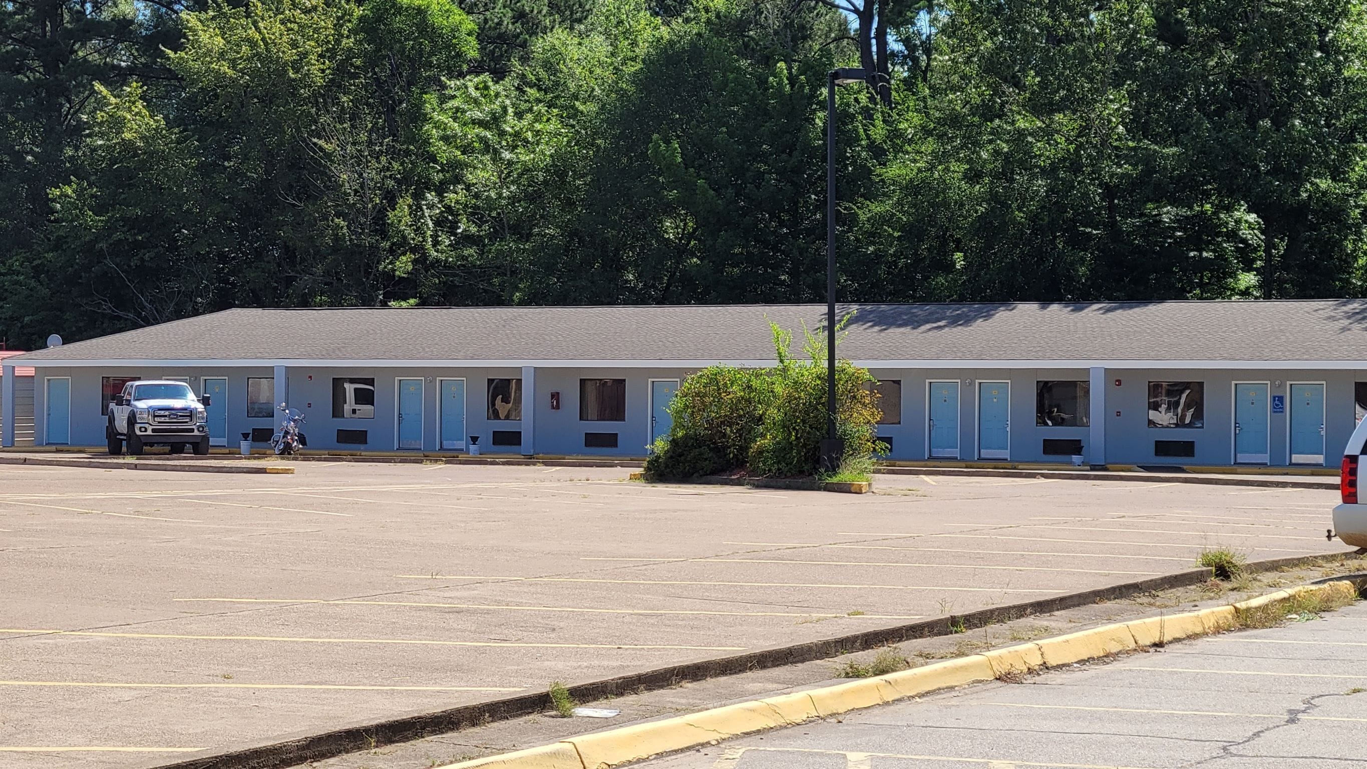 A motel with a row of rooms, a parking lot, and a small garden area.