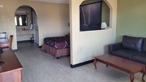 Una habitación de hotel con cama, sofá, mesa de madera, escritorio, baño con lavamanos y un ventanal con vistas.