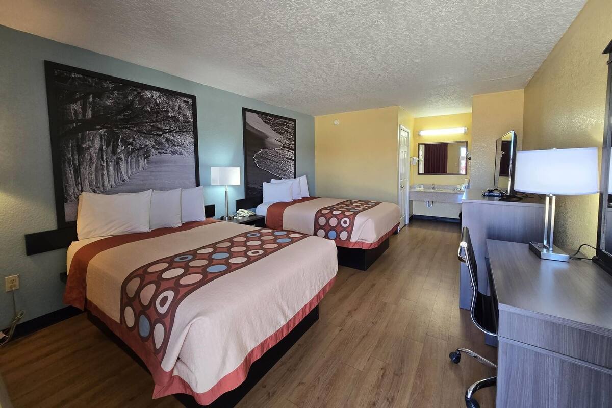 Une chambre d’hôtel avec deux lits, un bureau, une chaise, un miroir et des œuvres d’art accrochées aux murs.