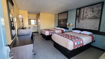 A hotel room with two beds, a desk, a chair, a mirror, and a large window.