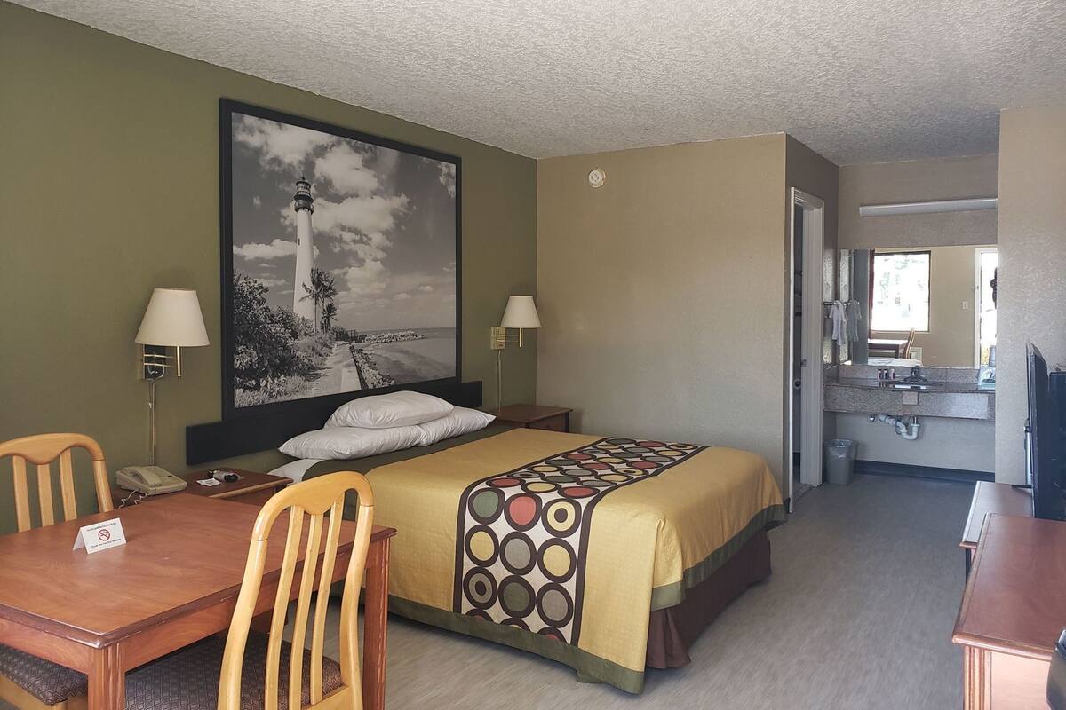 Une chambre d’hôtel comprenant un lit, un bureau, une chaise, un téléphone, une lampe et un grand tableau représentant un phare.