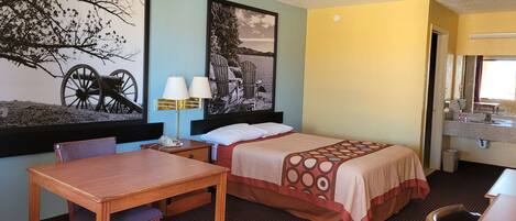 Habitación de hotel con una cama, un escritorio y dos sillas. Hay dos lámparas de pared y un cuadro con un árbol y una silla.