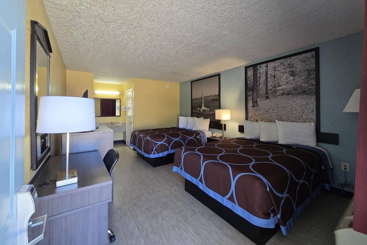 Une chambre d’hôtel avec deux lits, un bureau, un miroir et un grand tableau au mur.