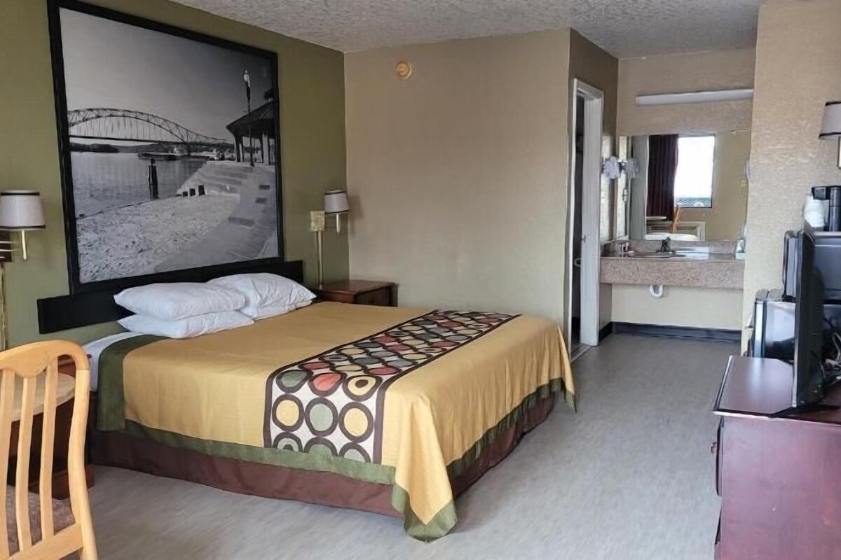 A hotel room with a bed, a desk, a chair, a television, and a bathroom visible through an open door.