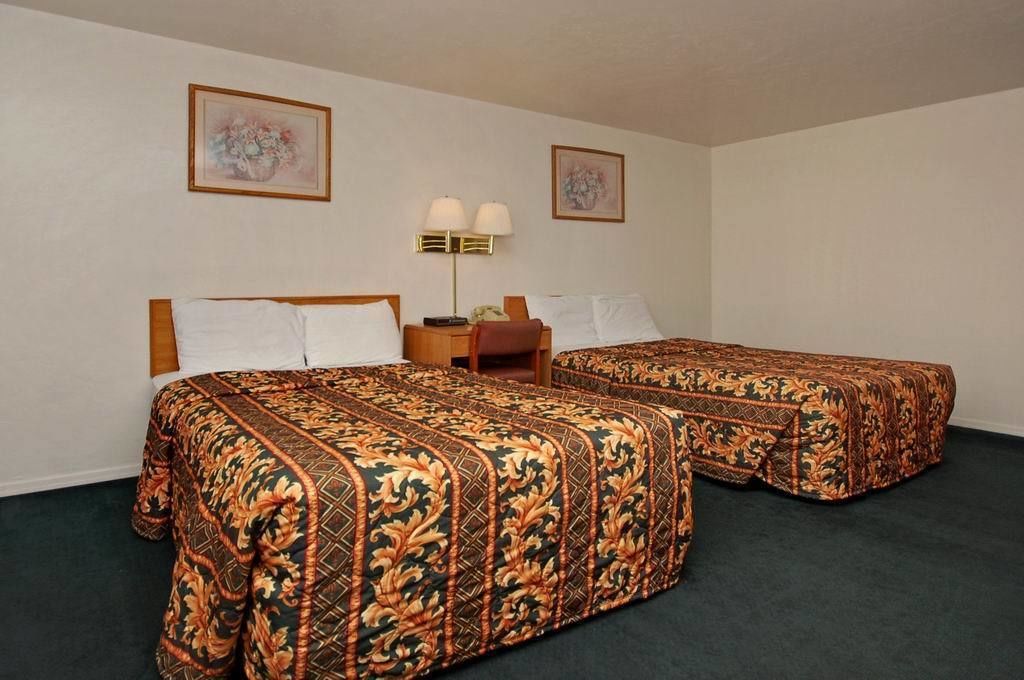 A hotel room with two beds, each with a floral-patterned bedspread, a bedside table with a lamp, and two framed floral paintings on the walls.