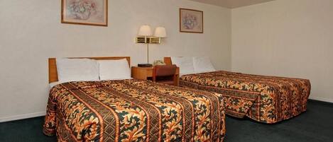 A hotel room with two beds, each with a floral-patterned bedspread, a bedside table with a lamp, and two framed floral paintings on the walls.