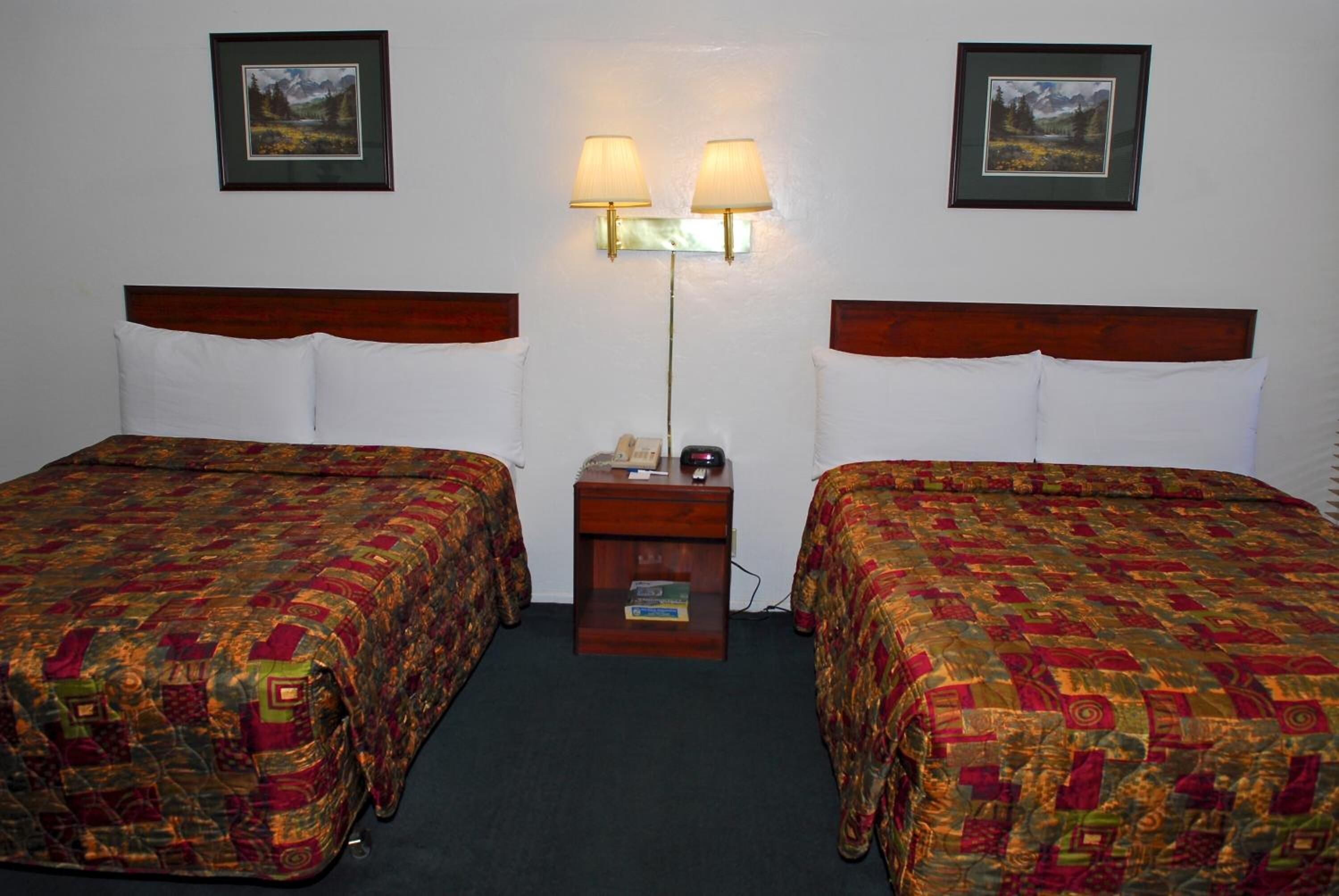 A hotel room with two beds, each with a patterned bedspread, a nightstand with a lamp, and framed pictures on the wall.