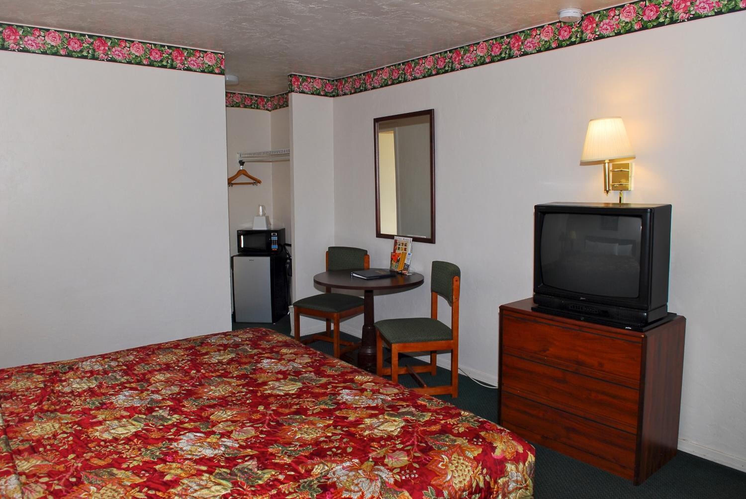A hotel room with a large bed, a small table with two chairs, a television on a wooden cabinet, and a mirror on the wall.