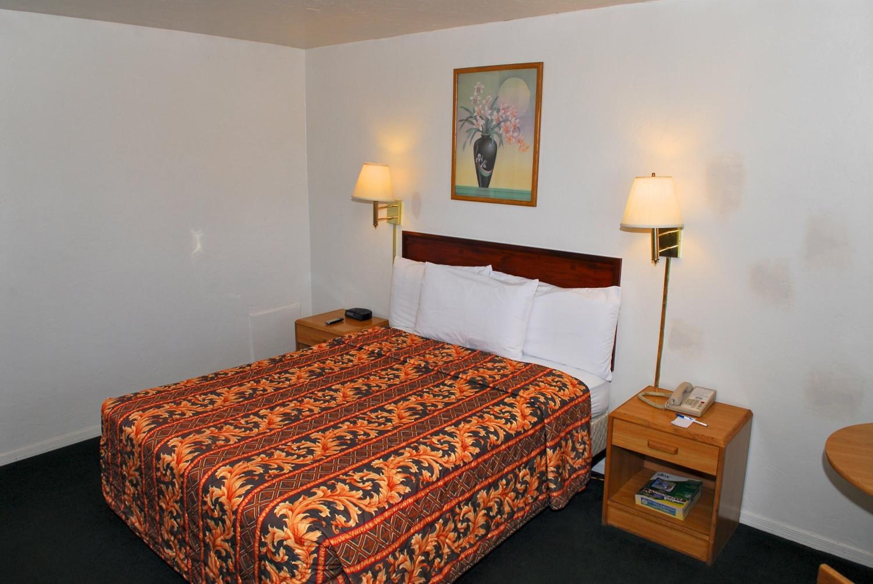 Habitació d'hotel amb un llit gran, dues làmpades de nit, una tauleta de nit amb un telèfon i un llibre, i un quadre a la paret.