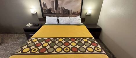 A hotel room with a bed, two bedside tables, a cityscape painting, and two wall-mounted lights.