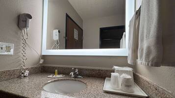 Une salle de bain d’hôtel avec un comptoir en granit, un lavabo, un miroir, un sèche-cheveux et des articles de toilette disposés sur un plateau.