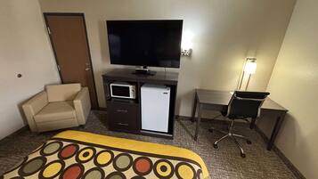 A hotel room with a bed, a desk, a television, a refrigerator, and a chair.